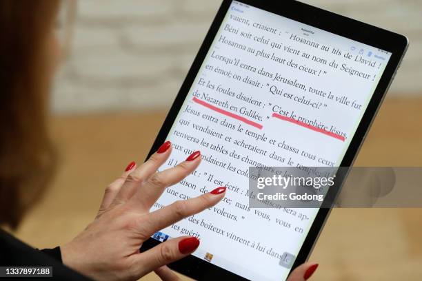 Woman reading and studying the gospels of the bible on a digital tablet Ipad. France.