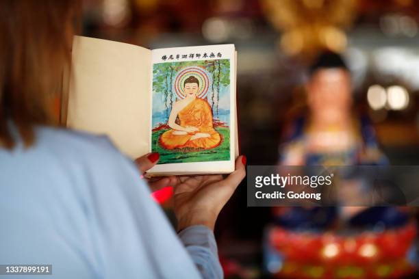 Thien Minh buddhist temple. Woman reading sacred buddhist texts. Shakyamuni Buddha illustration on the first page. France.
