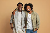 Portrait Of Two Happy Black Guys Embracing While Posing Over Beige Background