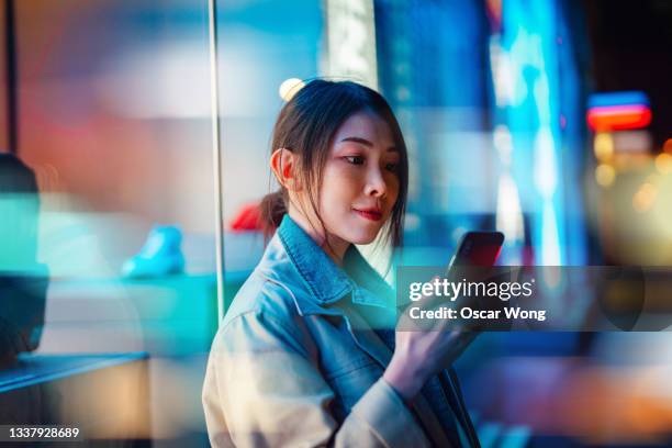 young woman standing and using smartphone  on city street with bokeh lights at the background - convenient store 個照片及圖片檔