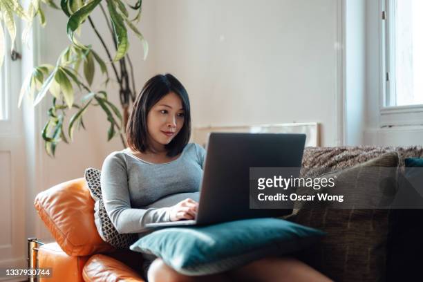 young pregnant businesswoman at home office, working with laptop on sofa - using laptop stock pictures, royalty-free photos & images