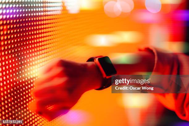 woman using smart watch against colourful neon light display - auf die uhr schauen stock-fotos und bilder