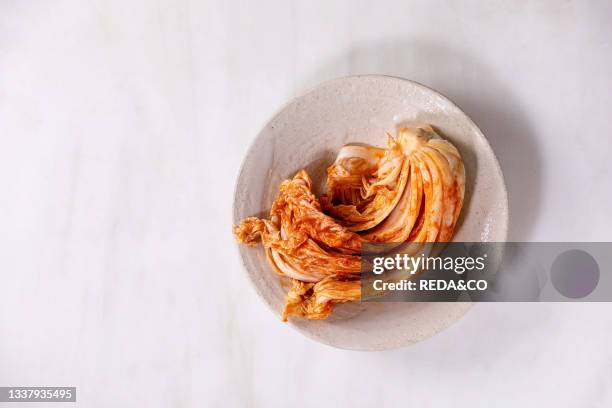 Homemade korean traditional fermented appetizer kimchi cabbage served in ceramic plate over white marble background. Flat lay. Copy space.
