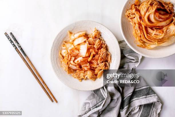 Homemade korean traditional fermented appetizer kimchi cabbage whole and chopped served in ceramic plate with chopsticks over white marble...
