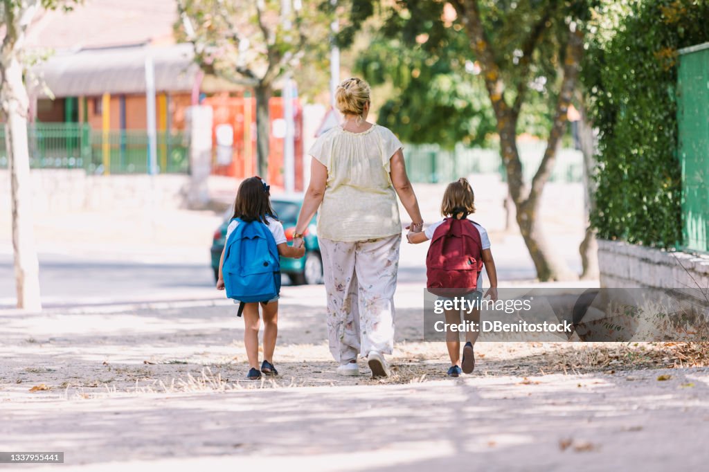 Mother and daughters with their backs turned, go hand in hand on the way to school. Concept of education and back to school.