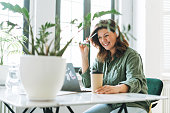 Young smiling brunette woman plus size working at laptop on table with house plant in the bright modern office