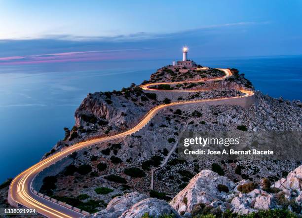 high angle view of light trails from cars on a road leading up to a lighthouse facing the sea at sunset. majorca island. - cabo formentor fotografías e imágenes de stock