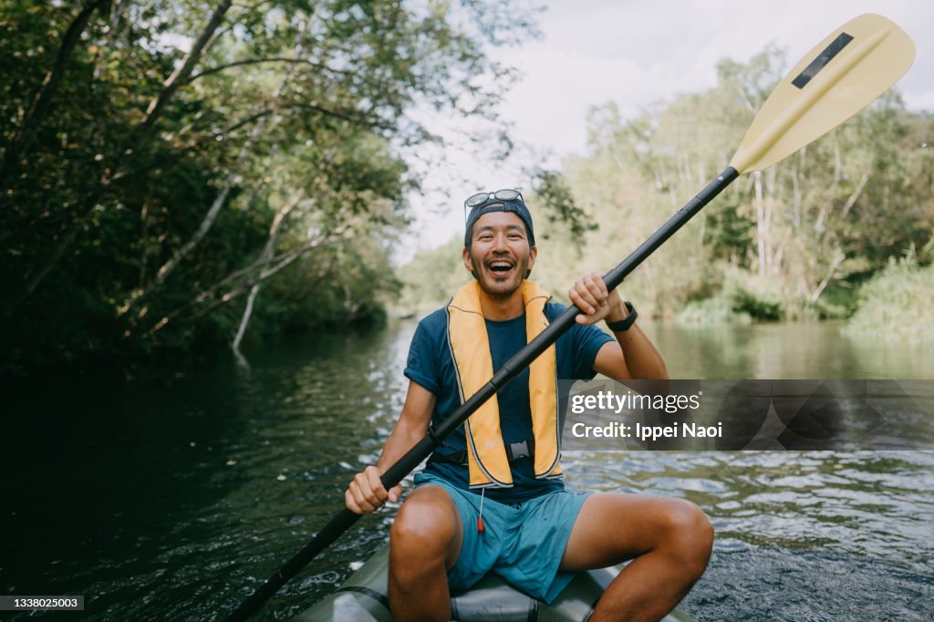 Cheerful man paddling kayak through river, Hokkaido, Japan