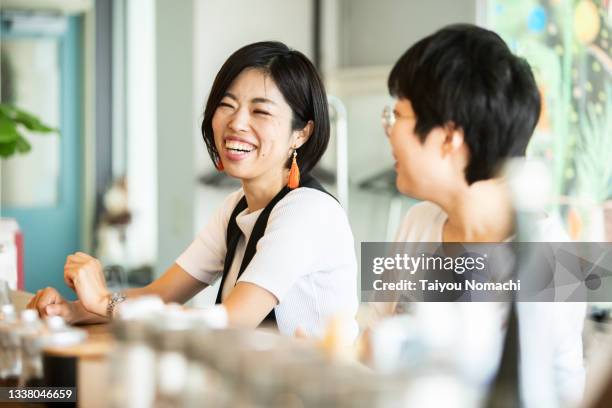 a woman talking with a friend at the counter of a cafe - japanese people photos et images de collection