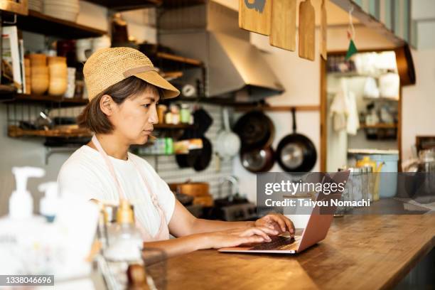 a woman owner of a vegan restaurant who stays at the restaurant to work on her laptop - small business laptop ストックフォトと画像