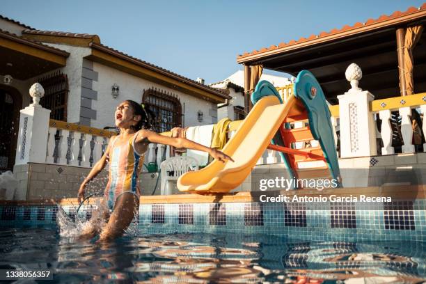 a young girl slips down the slide and falls into a swimming pool at her home during the summer - slide stock-fotos und bilder