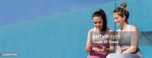 two women using smartphone to share social media after morning fitness workout. female friends with sport outfit in the morning - femininity stock pictures, royalty-free photos & images