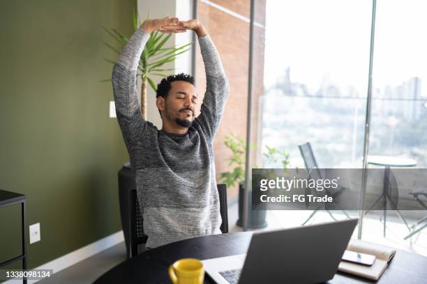 man stretching in the chair while using laptop at home - work routine imagens e fotografias de stock
