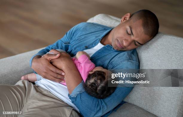 exhausted father sleeping on the sofa while holding his baby - father holding sleeping baby stockfoto's en -beelden