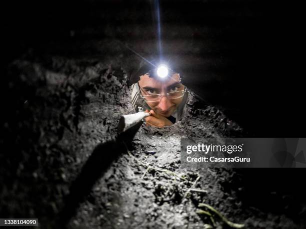 man with a head torch and a stick looking inside a hole - digging hole stock pictures, royalty-free photos & images