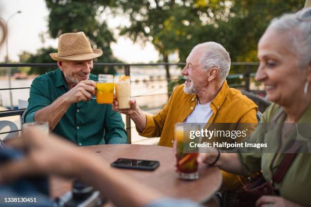 group of happy senior friends tourists sitting outdoors in sidewalk cafe in city, enjoying drinks. - senior men cafe stock pictures, royalty-free photos & images