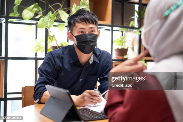 young chinese entrepreneur and his muslim business partner in hijab having meeting discussion using laptop in co-working environment. - business plan covid stock pictures, royalty-free photos & images