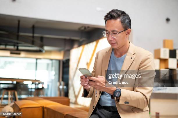 portrait d’un homme asiatique d’âge moyen en tenue d’affaires envoyant un message texte à son client au poste de travail - asian businessman phone photos et images de collection