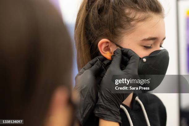 pre-teen girl getting ear pierced with needle, squeezing eyes closed - ear piercing stock-fotos und bilder