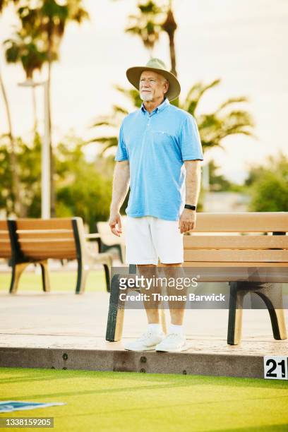 Wide shot of senior man watching partner bowl during lawn bowling match on summer evening