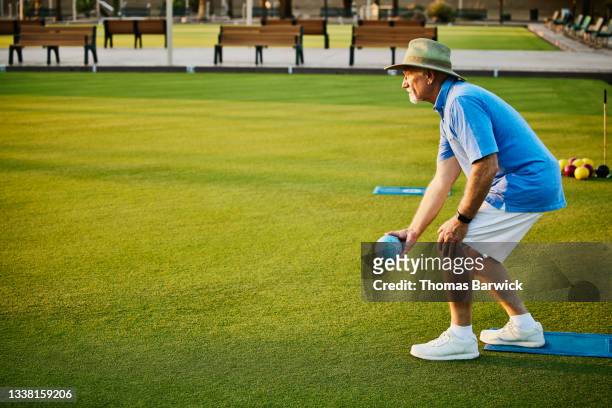 Wide shot of senior man preparing to throw bowl during lawn bowling match on summer evening