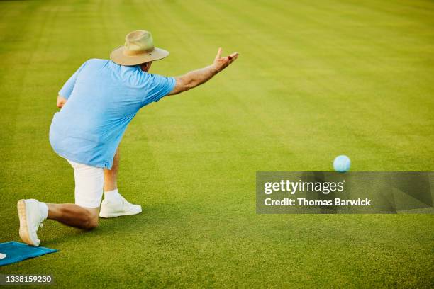 Wide shot of senior man throwing bowl during lawn bowling match on summer evening