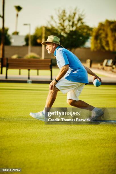 wide shot of senior man throwing bowl during lawn bowling match on summer evening - senior men bowling stock pictures, royalty-free photos & images