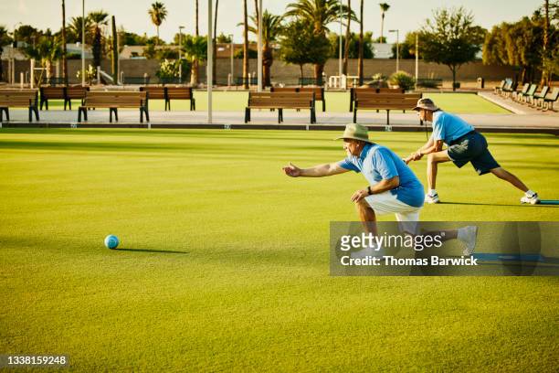 Wide shot of senior men bowling during lawn bowling match on summer evening