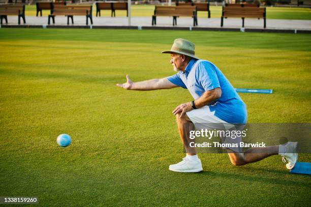 wide shot of senior man throwing bowl during lawn bowling match on summer evening - seulement des hommes seniors photos et images de collection