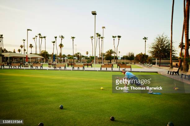 Extreme wide shot of senior man throwing bowl during lawn bowling match on summer evening