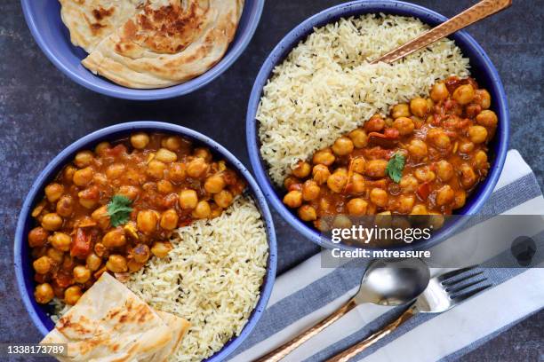 image blue plates homemade punjabi chole (chickpea curry) meal, white rice, lachha paratha (flatbread), spoon, fork, striped tea towel, mottled blue background, elevated view - curry leaves stockfoto's en -beelden