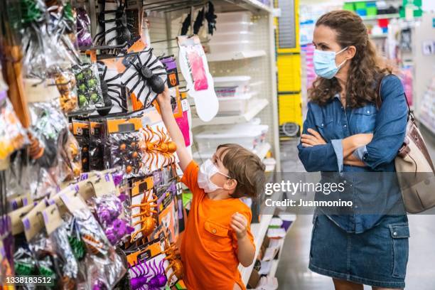 little boy shopping for halloween toys wearing a protective face mask - toy store stock pictures, royalty-free photos & images