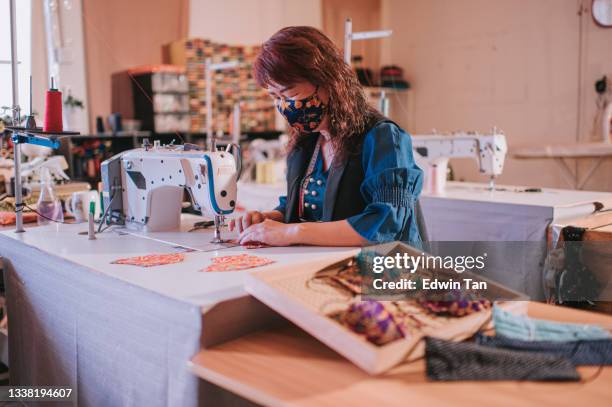 asian chinese senior woman entrepreneur tailor sewing batik protective face mask in front of sewing machine at studio work place - safety pin stockfoto's en -beelden