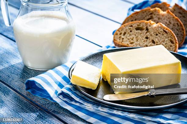 butterstange, milchglas und brot auf blauem tisch - butter stock-fotos und bilder