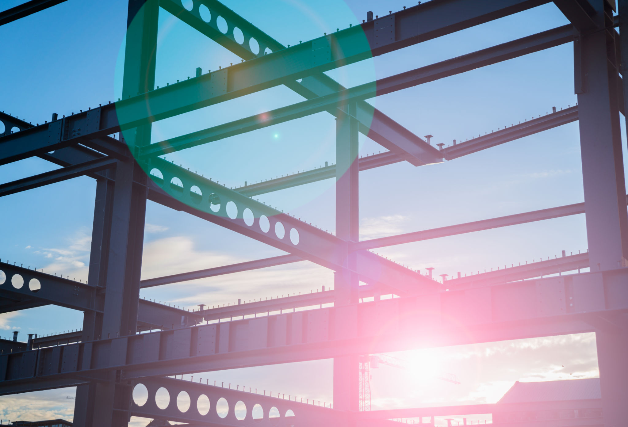 Sunrise lens flare through construction steel framework in silhouette against blue sky Sunrise lens flare through construction steel framework in silhouette against blue sky