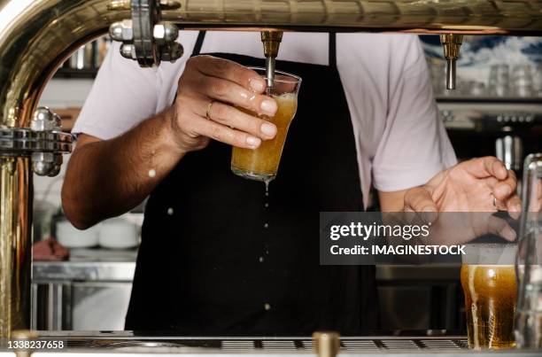 barman filling beer from the tap at the bar - camarero fotografías e imágenes de stock