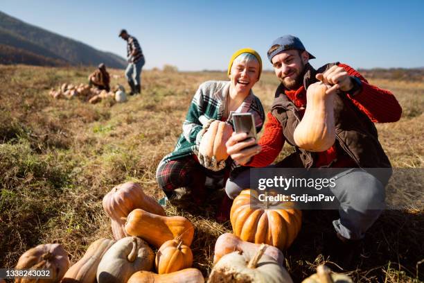 cheerful caucasian couple making selfie with the smart phone with pumpkins after harvesting - pumpkin patch stock pictures, royalty-free photos & images