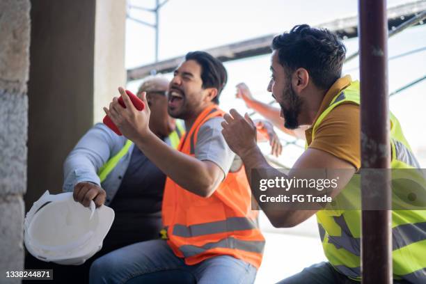 construction workers watching sports match on smartphone in a construction site - euphoria stock pictures, royalty-free photos & images