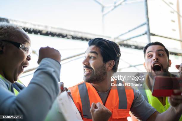 bauarbeiter, die sport auf dem smartphone auf einer baustelle verfolgen - industrial fan stock-fotos und bilder