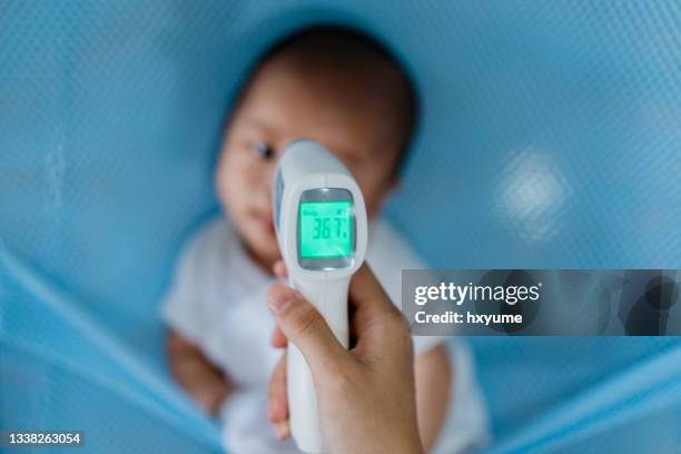 mother checking body temperature of her baby - temperature gun stock pictures, royalty-free photos & images