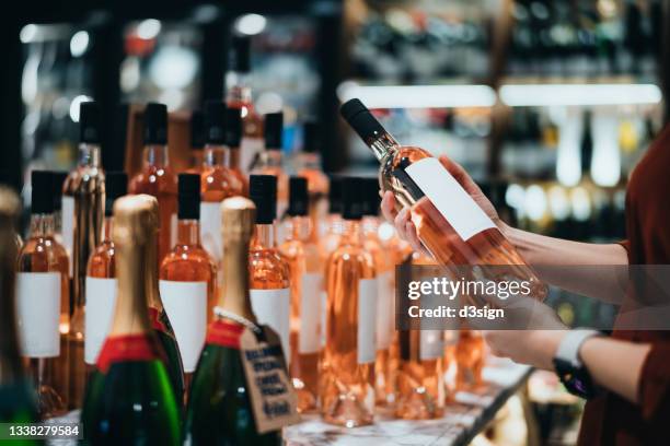 close up of young asian woman walking through liquor aisle and choosing a bottle of rose wine from the shelf in supermarket - vino rosado fotografías e imágenes de stock