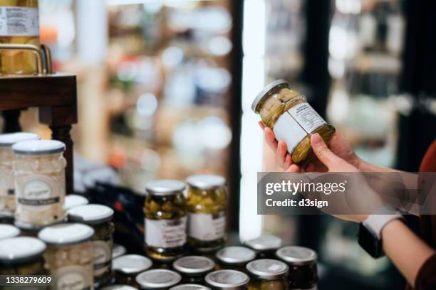 close up of young asian woman grocery shopping in supermarket, holding a bottle of preserved vegetable and reading the nutrition label. making healthier food choices - nutrition label stock pictures, royalty-free photos & images