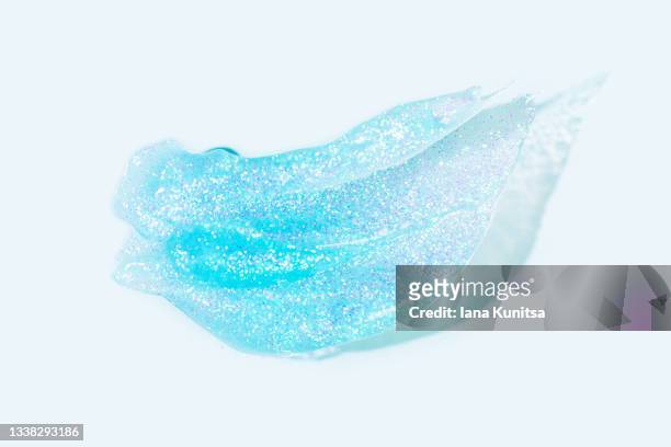 transparent glitter gel is smeared on blue background. beauty face serum texture. hydrating hyaluronic acid. cosmetic products for makeup and skin care. cosmetology. - lip gloss smudge stock-fotos und bilder