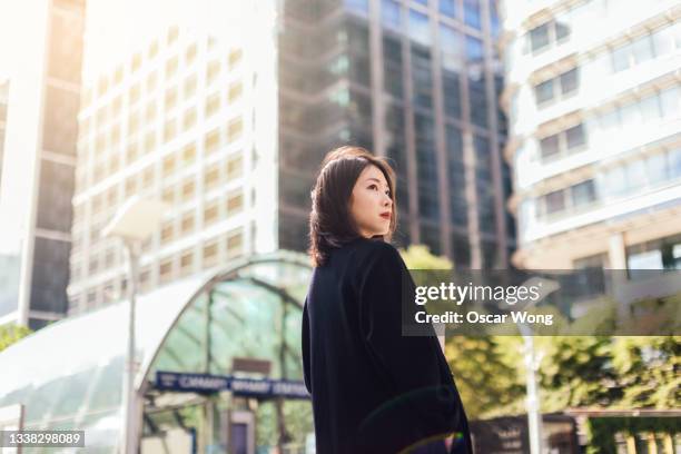 young woman having coffee break and walking in city against modern commercial buildings - business woman looking over shoulder stock pictures, royalty-free photos & images