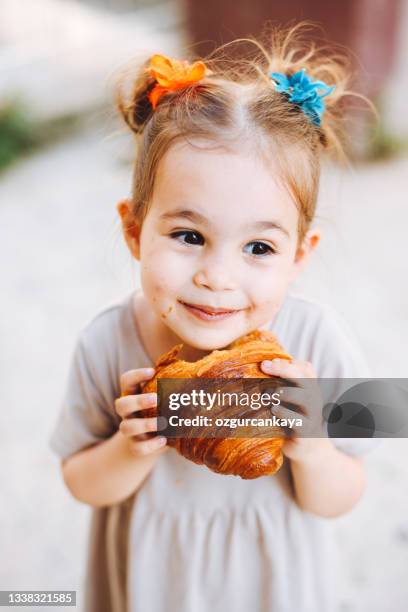 little girl with blond hair eating crispy croissant outdoors on street - eating croissant stock pictures, royalty-free photos & images