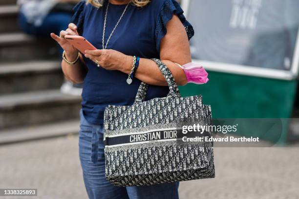 Guest wears a navy blue with cut-out sleeves t-shirt, blue flowing pants, a blue and beige Dior Oblique Jacquard Book Tote handbag from Dior, a...