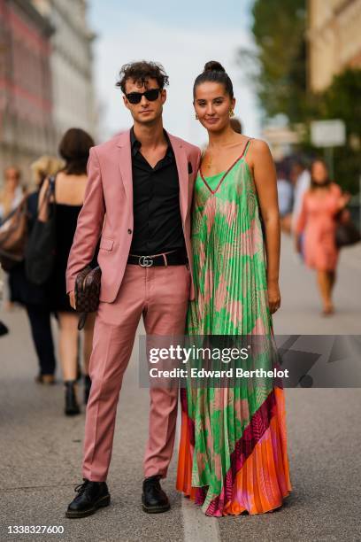 Guest wears black sunglasses, a black shirt, a pale pink blazer jacket, matching pale pink suit pants, a black shiny leather with silver GG buckle...