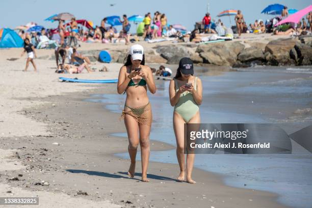 Two women looking at their phones walk along Rockaway Beach over Labor Day Weekend on September 4, 2021 in the Queens Borough of New York City. Some...