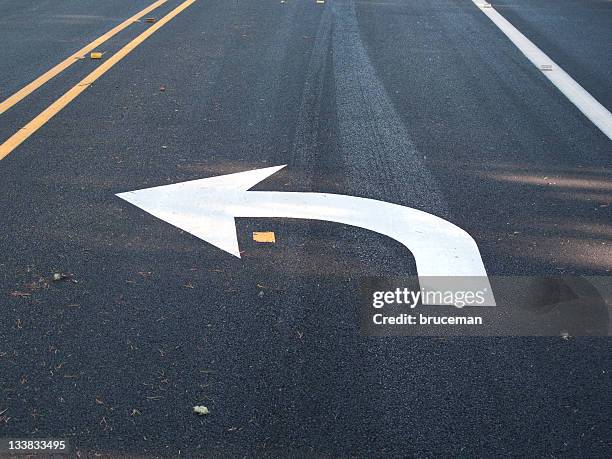 white turn left arrow painted on asphalt - median signs stock pictures, royalty-free photos & images