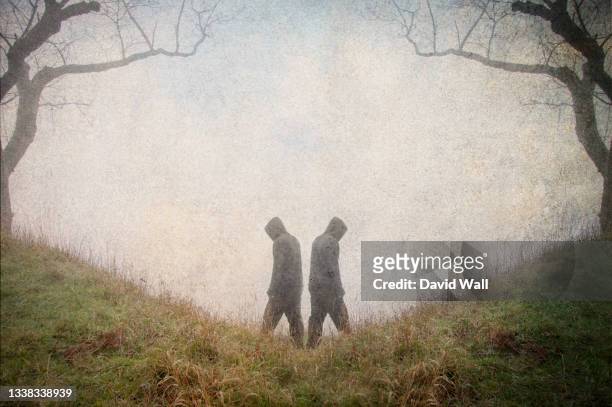 a mysterious double exposure of a symmetry of two hooded figures. standing in a spooky forest on a hill, on a misty winter's day. - dubbelgångare bildbanksfoton och bilder